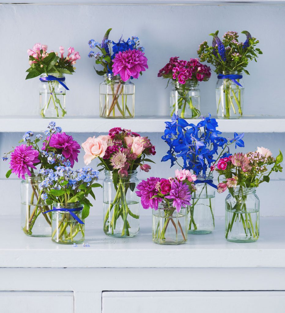 Clear glass jars tied with bright blue ribbons and filled with fresh flowers in shades of blue and pink. 