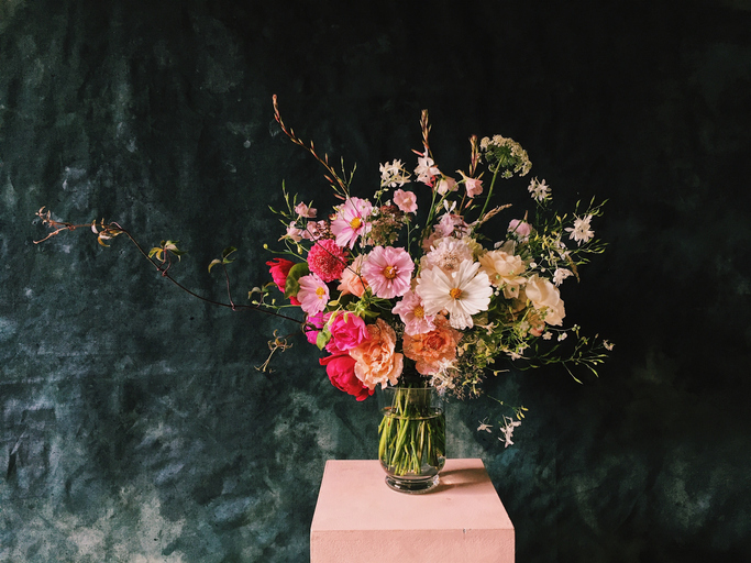 Dark backdrop with a tall pink box topped with a floral arrangement. 