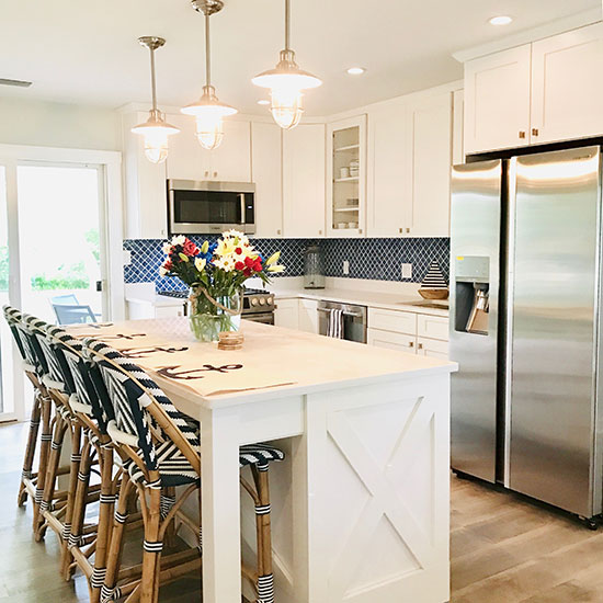 Modern farmhouse kitchen with a coastal vibe. White cabinets and stainless steel appliances with Parisian bistro woven barstools. 