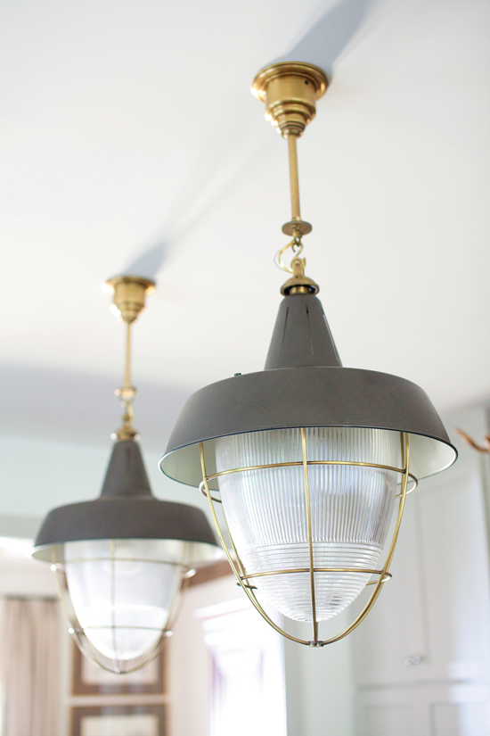A pair of slate gray pendant lamps hanging from gold hardware. 