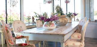Shabby chic inspired dining room with rustic looking table and chairs and fresh flowers as a centerpiece.