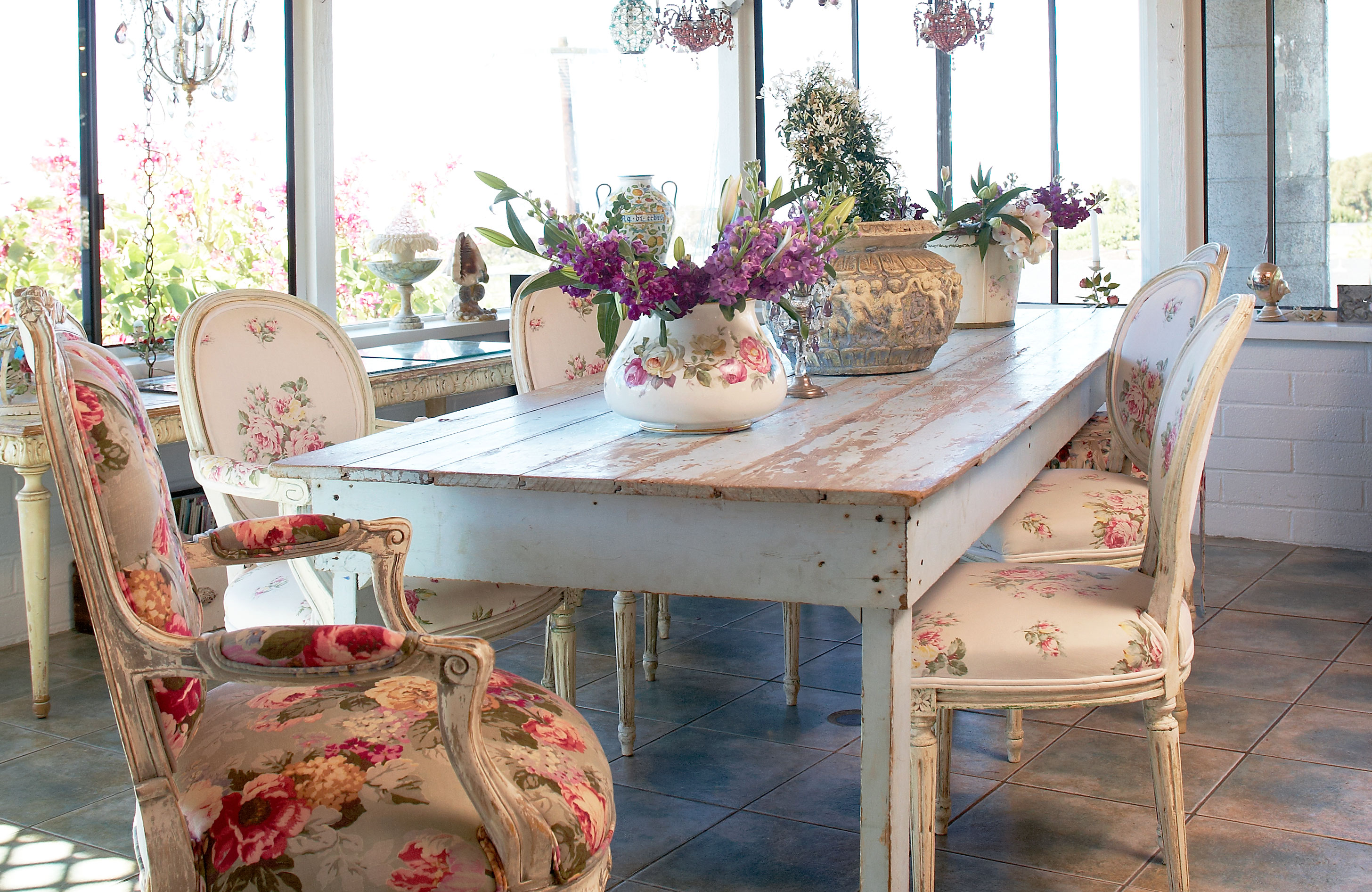 Shabby chic inspired dining room with rustic looking table and chairs and fresh flowers as a centerpiece.