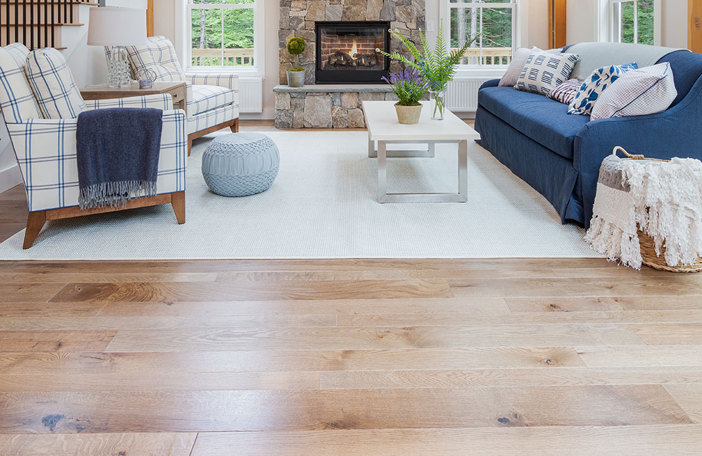 Cozy cottage living room with hardwood floors, white rug and blue and white couch and armchairs in front of a fireplace. 