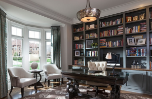 Home office with regal wooden desk, bright bay window and a wall of books.