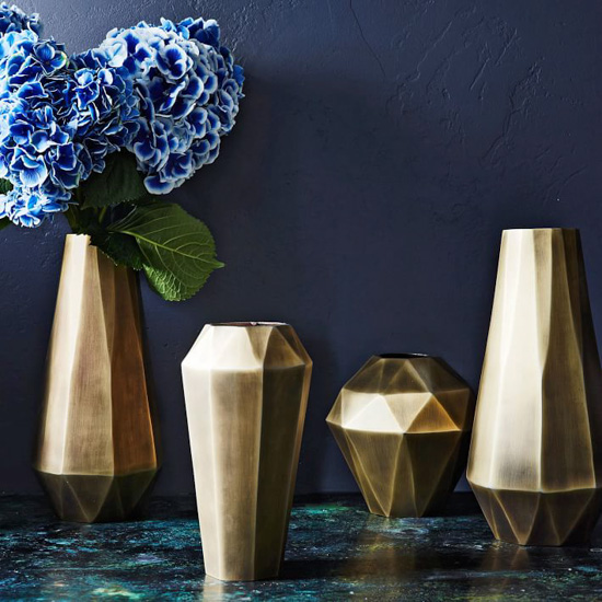 Gold geometric style vases in varying sizes, one filled with blue hydrangeas. 
