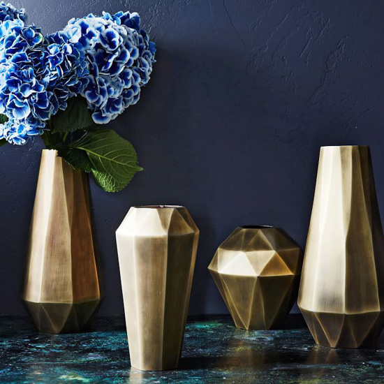 Gold geometric style vases in varying sizes, one filled with blue hydrangeas.