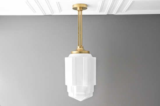 Gray wall and textured white ceiling with a white hanging pendant lamp and gold hardware. 