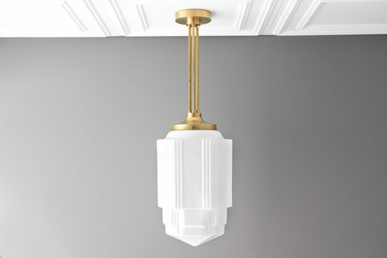 Gray wall and textured white ceiling with a white hanging pendant lamp and gold hardware.