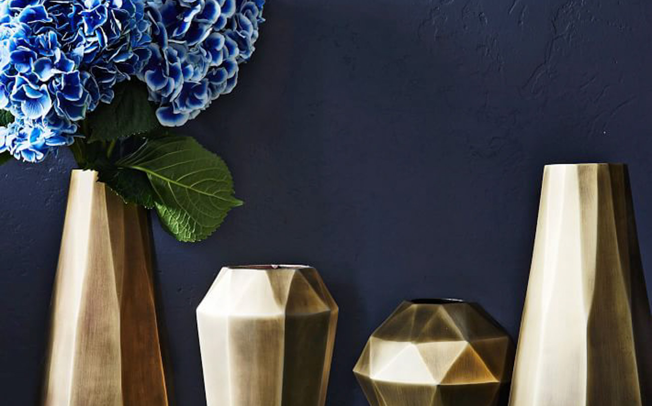 Gold geometric style vases in varying sizes, one filled with blue hydrangeas.