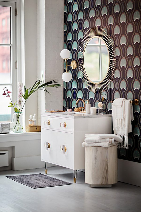 Modern styled bathroom with Art Deco patterned wallpaper under a sunburst mirror with white furniture. 