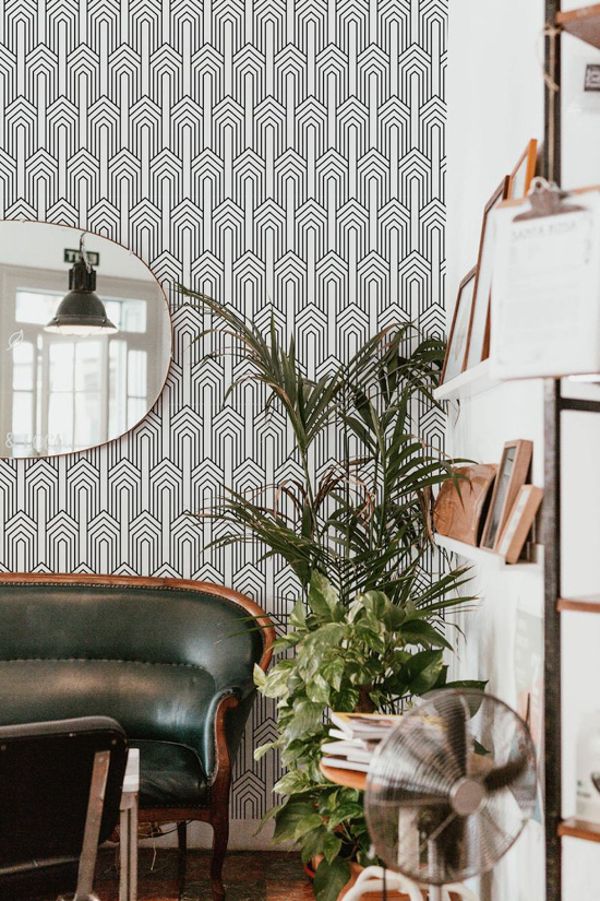 Art Deco patterned black and white wall paper in a study with bookshelves, large plant and leather couch.