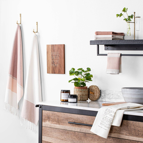 Kitchen counter with wooden rustic drawers and rose and cream colored hand towels on display alongside fresh greenery. 