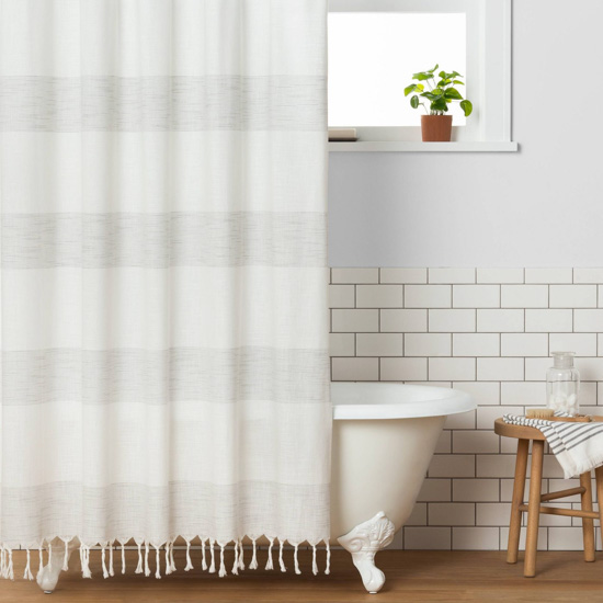 White clawfoot tub under a window, displaying a light striped woven shower curtain.