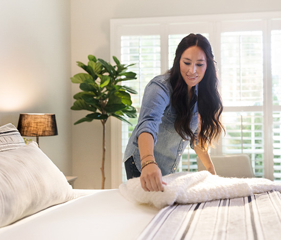 Joanna Gaines adding finishing touches to a bed display with a fiddle leaf fig tree in the background. 