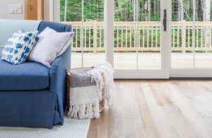 Blue couch with light throw pillow and basket of blankets next to it and hardwood floors leading to an outdoor balcony.