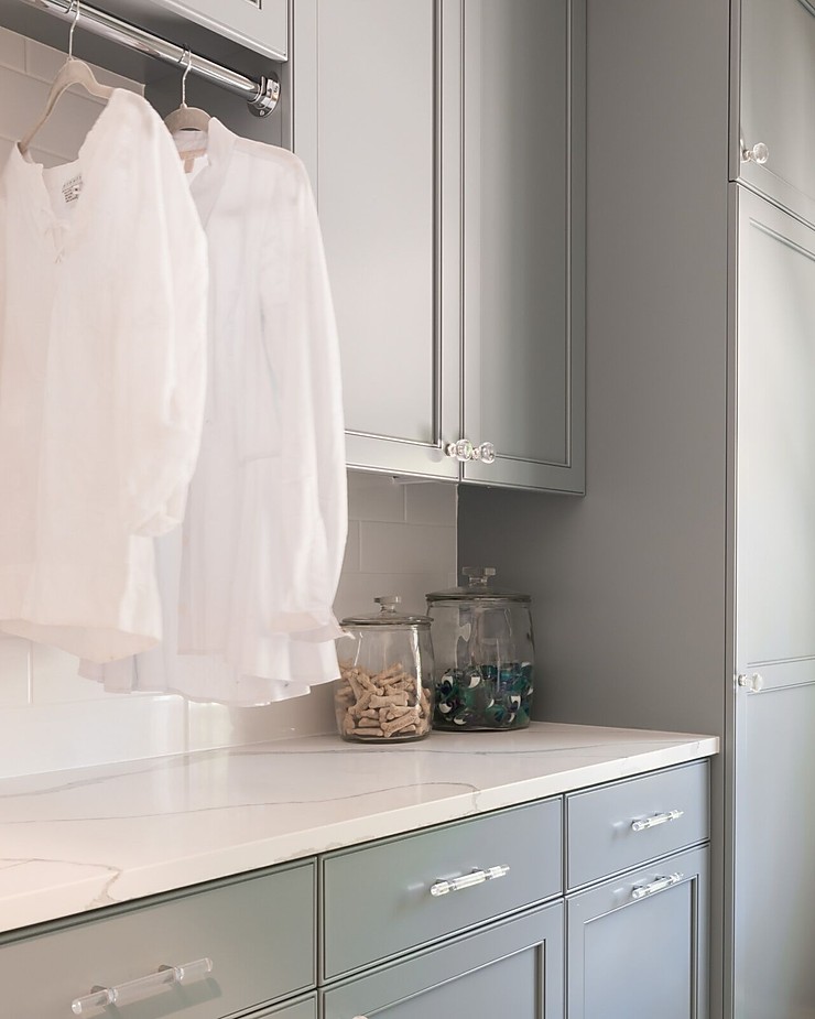 Light blue gray cabinetry with white marble countertop and white shirts hanging to dry. 