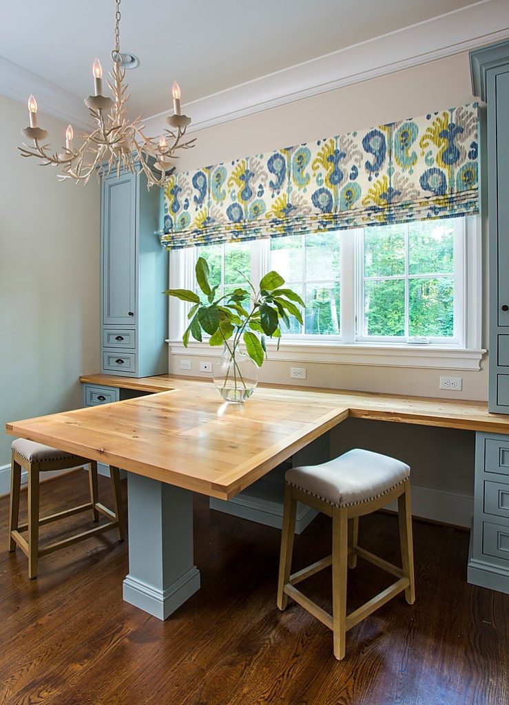 Shared desk space in a home office, with upholstered stools and a white chandelier and blue cabinetry.