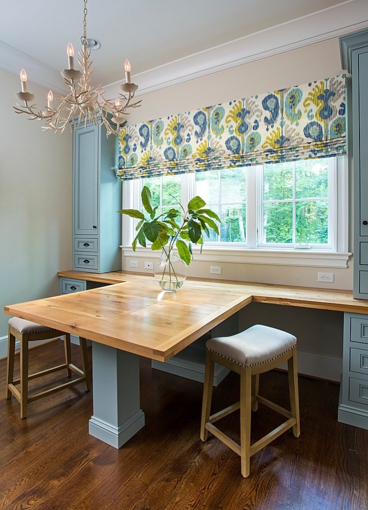 Shared desk space in a home office, with upholstered stools and a white chandelier and blue cabinetry. 