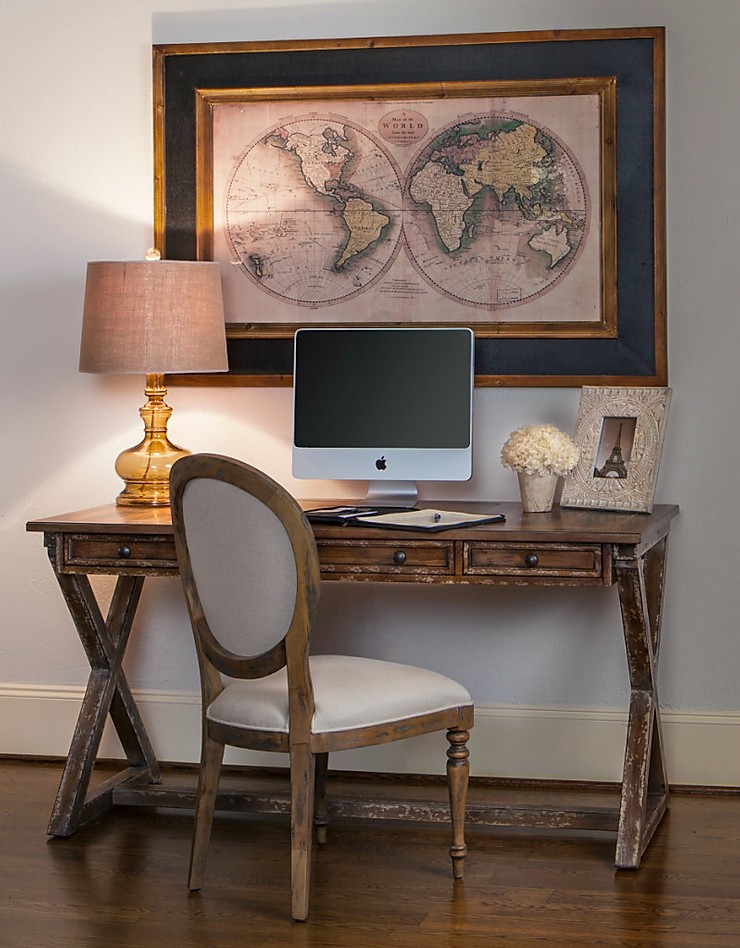 Intimate home office space with apple desktop computer, wooden desk and chair and framed and matted atlas print hanging above it. 