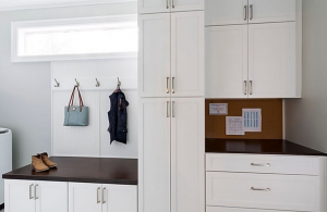 White cabinetry in a customized mudroom with long rectangular window, hanging hooks and cork board.