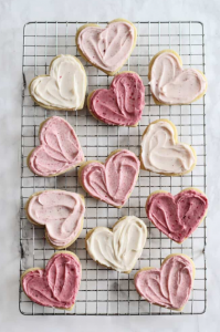 Cooling rack covered in ombre heart shaped sugar cookies with shades of pink frosting.