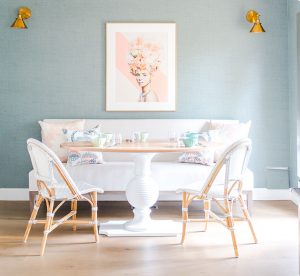 small dining area with sage green walls, a linen love seat and two french bistro chairs around a round table.