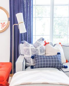 A corner of Rachel Shingleton's couch with classic blue pillows and trim in a pop of bright red-orange coral.