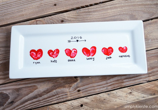 White ceramic rectangular platter Valentine's crafts with heart-shaped thumbprints, laying on a wooden table. 