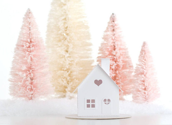 Pink and cream bottle brush trees with fake snow and a white paper crafted house with heart cutouts.