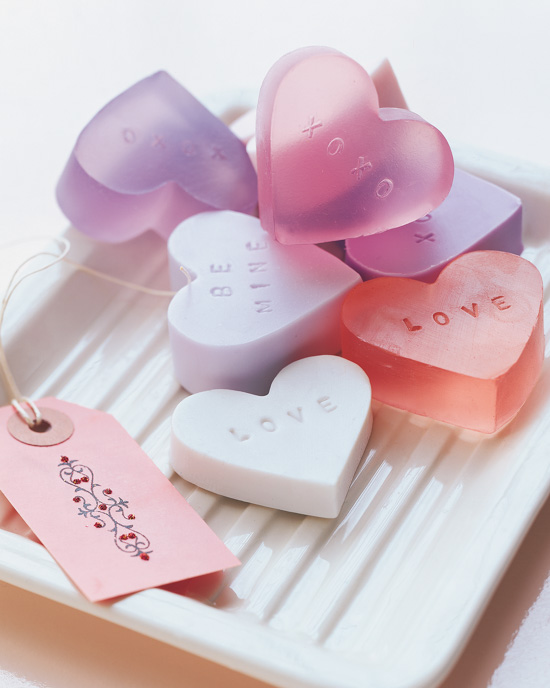 Handmade heart-shaped soaps in the shape of a heart and placed in a stack on a white glass tray. 