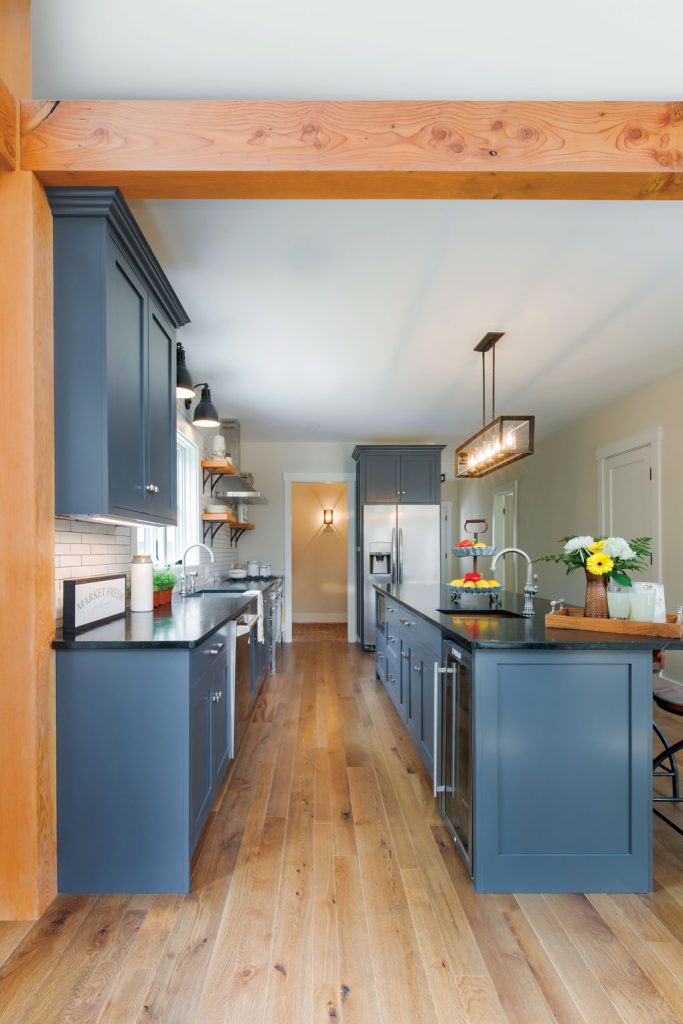 Wooden beams accent the open galley kitchen with blue shaker cabinets and stainless steal appliances.