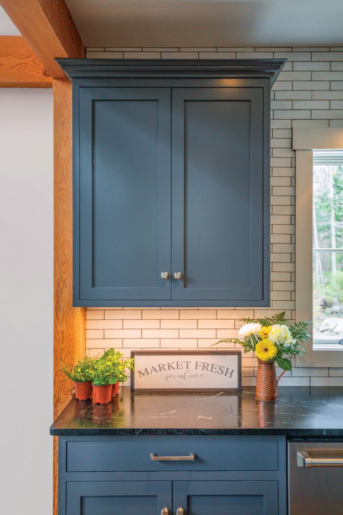 Dark soapstone countertops with white subway style backsplash and fresh flowers on the counter, surrounded by blue shaker cabinets in the kitchen. 