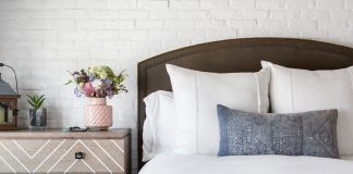 the whole house deep clean. A bedroom with a walnut arched headboard, clean white linens and an indigo duvet. A germanschmear brick wall pops behind the headboard. . The