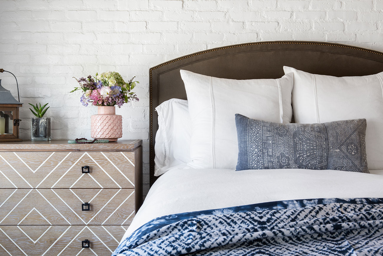 the whole house deep clean. A bedroom with a walnut arched headboard, clean white linens and an indigo duvet. A germanschmear brick wall pops behind the headboard. . The
