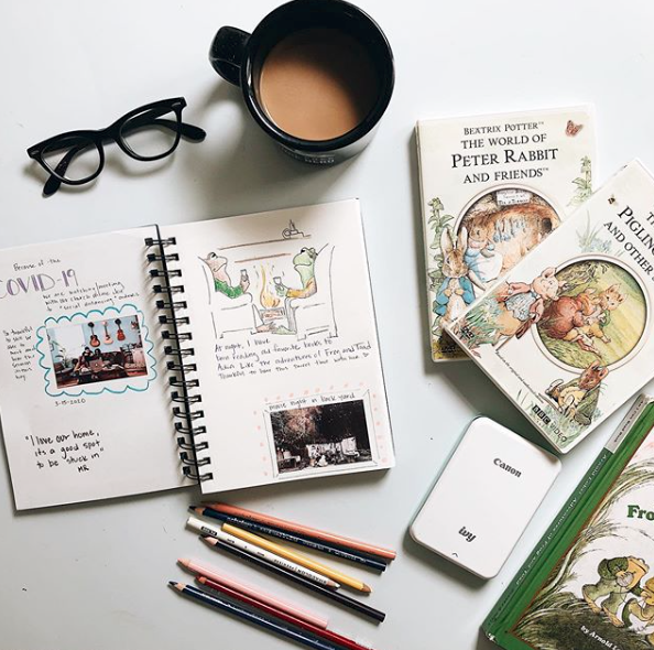 Coffee mug, reading glasses, art supplies and childrens classic books spread out on a table. 