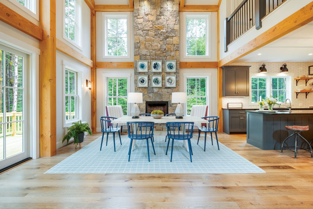 Expansive and open dining room with wood beaming framing the walls and looking into a kitchen with dark blue cabinetry. 