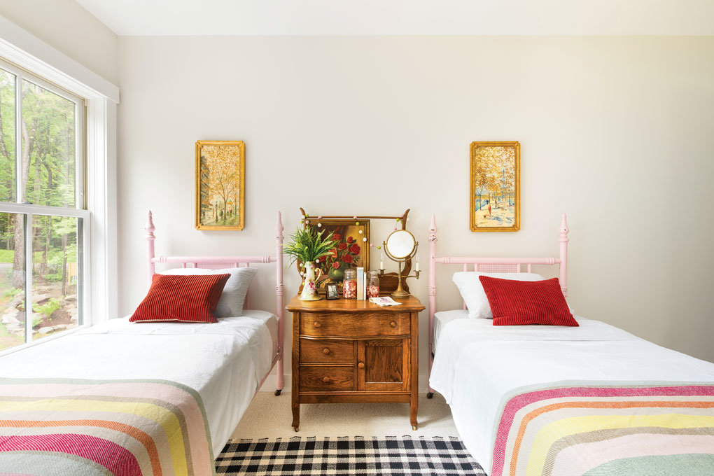 Traditional twin beds in a soft pink with striped throw blankets separated by a vintage wooden bedside table. 