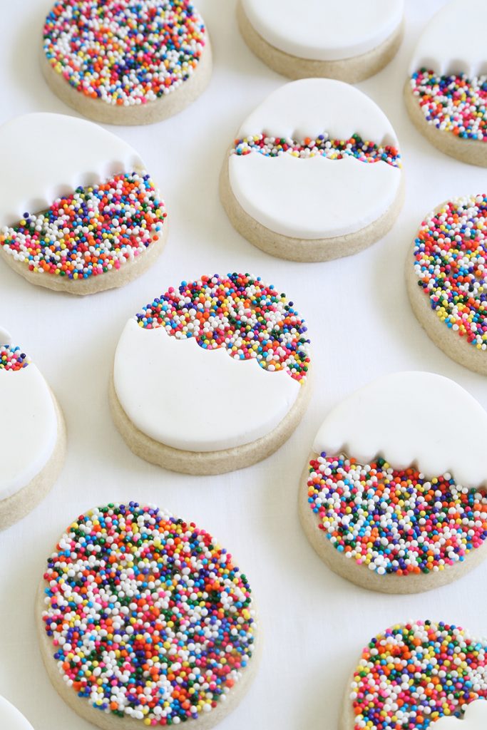 Tray of sugar cookie Easter desserts in the shape of eggs topped with decorative frosting and rainbow sprinkles.