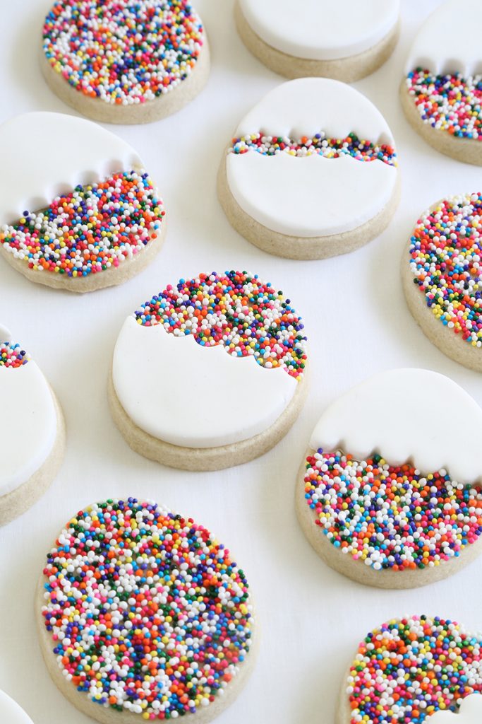 Tray of sugar cookie Easter desserts in the shape of eggs topped with decorative frosting and rainbow sprinkles. 