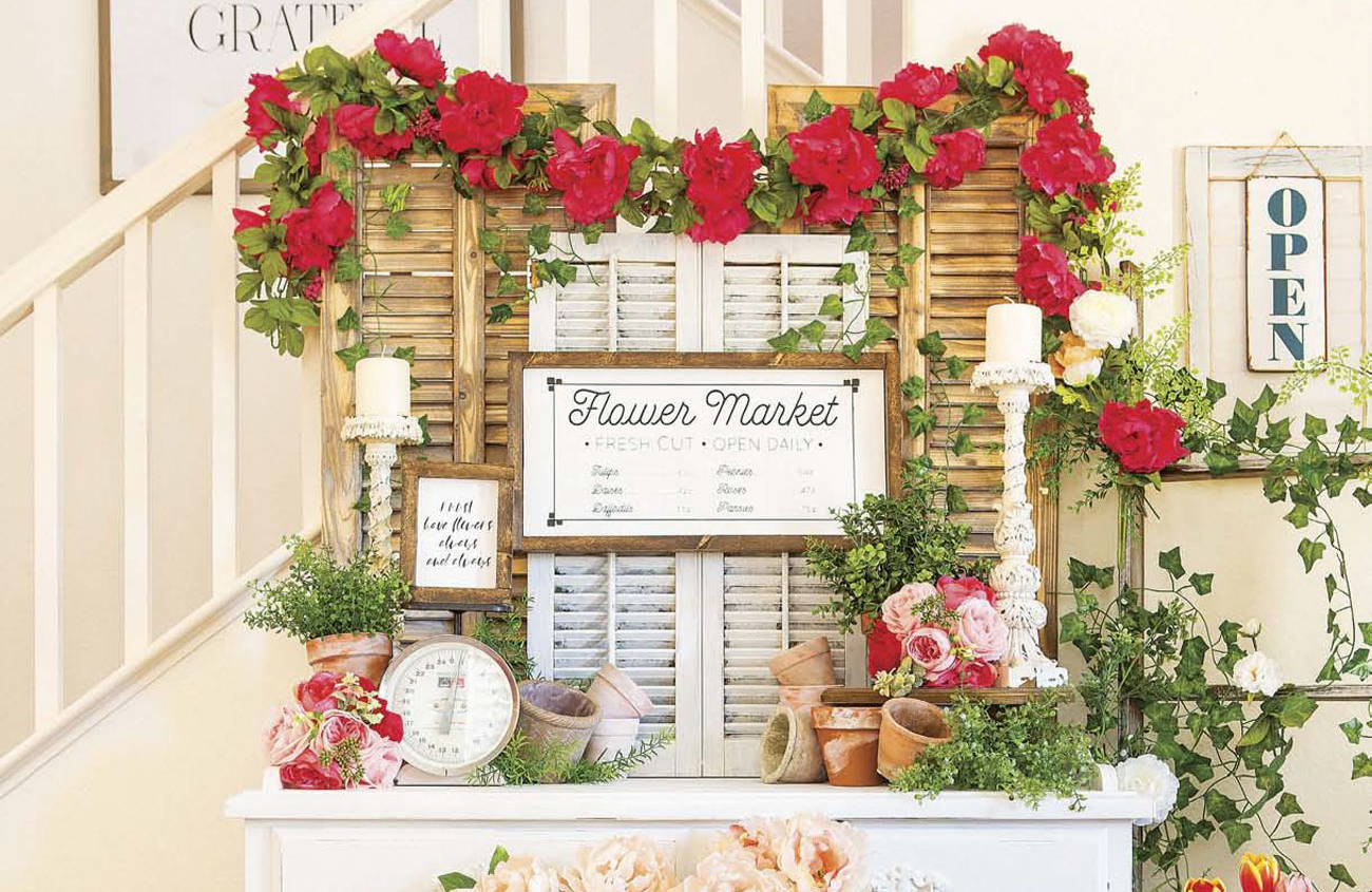 Faux flower market made up of a white dresser and shutters and a copious amount of fresh flowers.