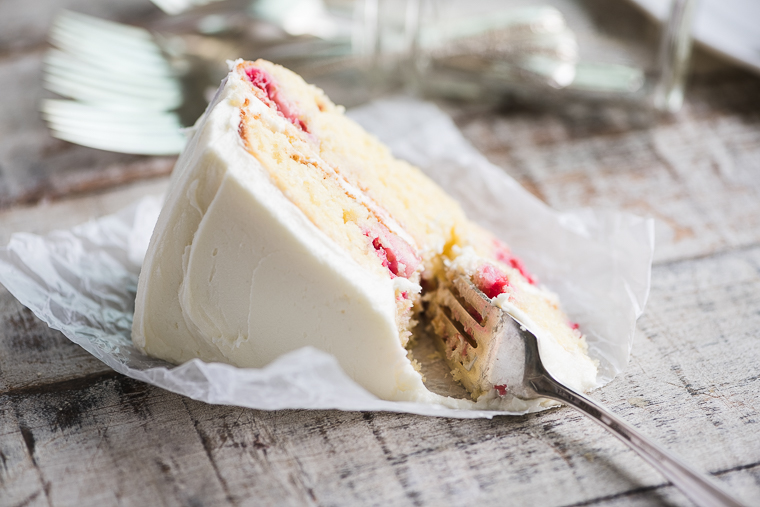 A slice of raspberry lemon cake laying on a rustic table with a ready bite on a fork.