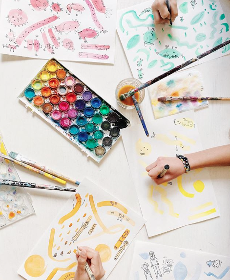 Watercolors, paintbrushes and kid hands making colorful art.