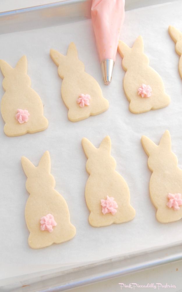 Silver baking tray covered in sugar cookie bunnies with pink frosting tails for a yummy Easter dessert. 