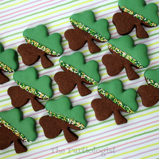 St. Patrick's Day Desserts shamrock shaped chocolate shortbread cookies half-dipped in green chocolate with a sprinkle stripe. 