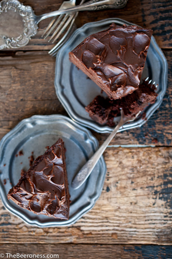 Metallic plates and silver forks displaying large slices of chocolate cake with chocolate frosting. 