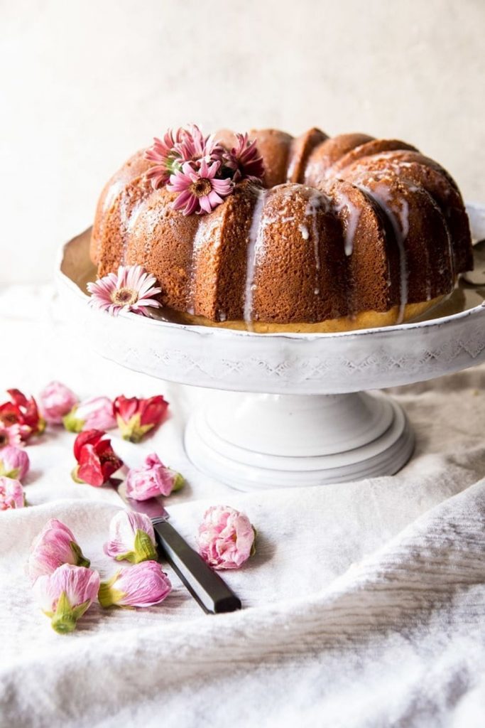 Cake stand with a brown bundt cake topped with drizzle frosting and fresh spring flowers.