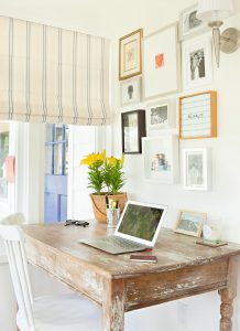 a small home office with a chippy vintage desk and charming homespun artwork on the wall