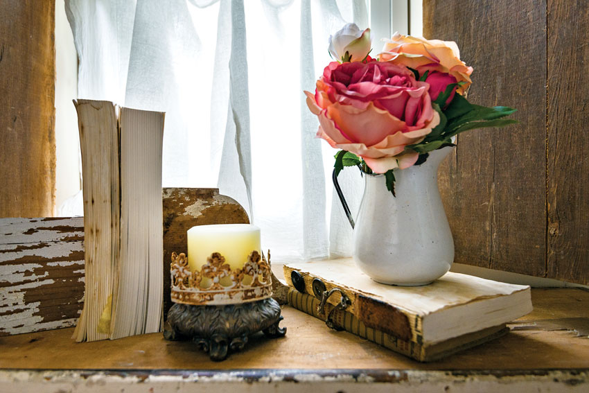 Table vignetter with old books, coral roses in white vase with a candle [A cozy country cottage]