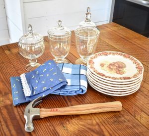 Hammer, plates, apothecary jars, and towels on a wood surface