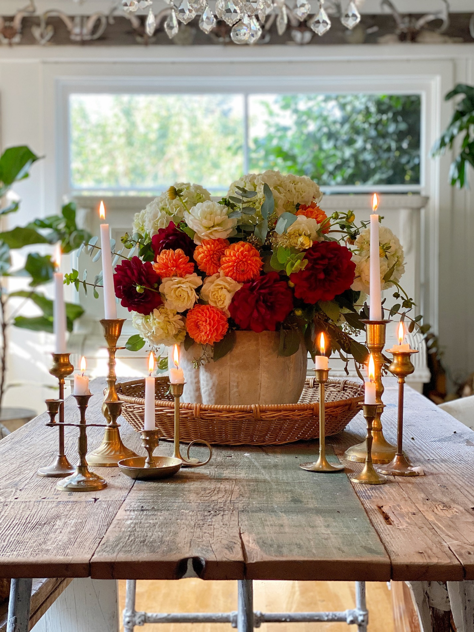 Cement pumpkin bowl sits on a wood table, filled with flowers and surrounded by vintage candles.